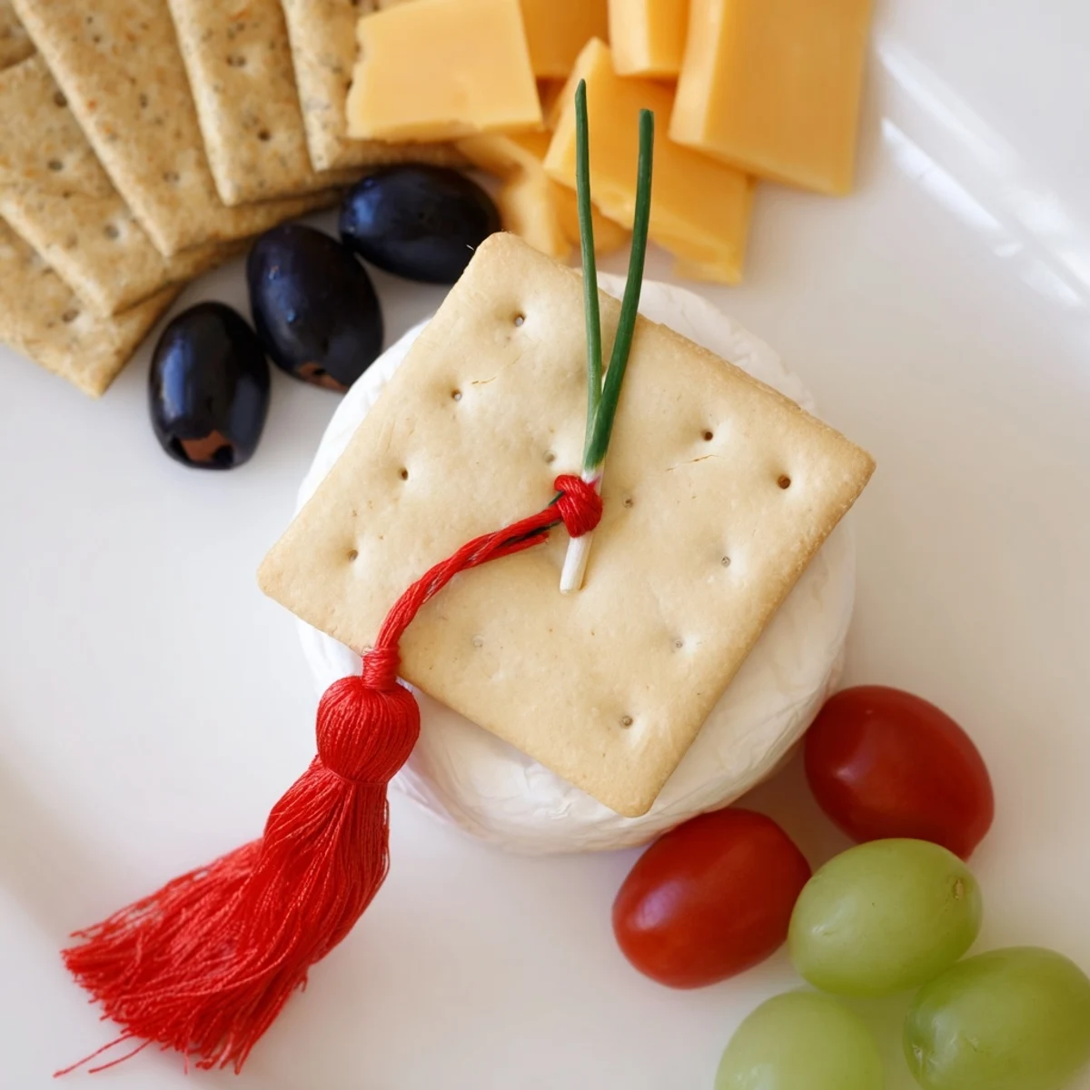 Graduation Cap Platter features a square cracker "mortarboard" with a red pepper tassel and vibrant fresh garnishes.