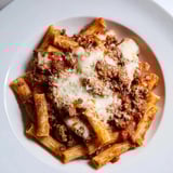 A close-up of a warm, comforting Cheesy Beef & Penne Bake, served with pasta and melted cheese.