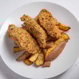 Close-up of crispy, flavorful Herbed Chicken Tenders alongside seasoned, baked potato wedges; a family favorite.