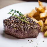 Juicy peppercorn ribeye, resting on a plate with golden fries, drizzled with savory peppercorn sauce.