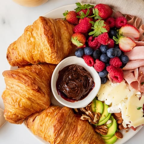 Flaky Cozy Fireplace Croissant Board overflowing with berries, cheeses, and warm, delicious croissants.