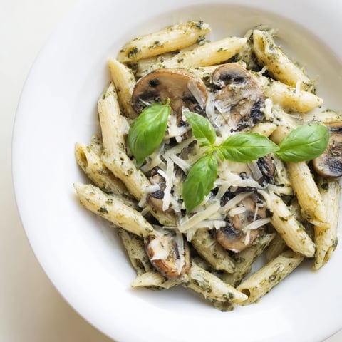 Golden penne pasta tossed in a creamy, vibrant green basil pesto sauce, topped with sautéed mushrooms and fresh basil leaves for a comforting, vegetarian main dish.