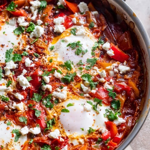 Steaming Shakshuka in a skillet with poached eggs nestled in a spiced tomato and pepper sauce.