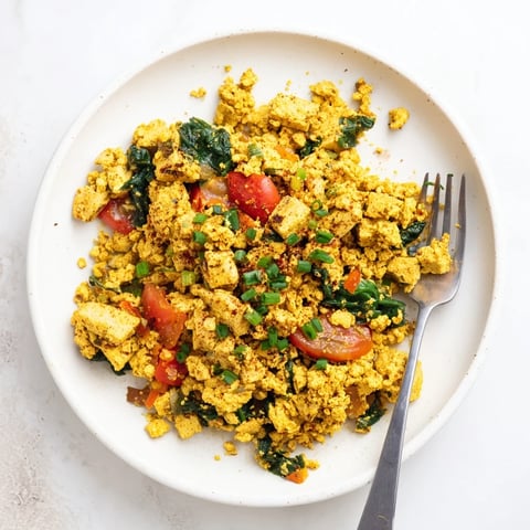 Golden turmeric tofu scramble with diced red bell peppers, onions, spinach, and fresh chives served in a rustic skillet.  