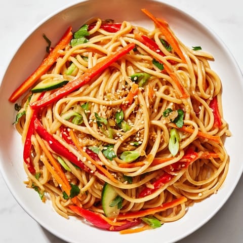 A close-up of a refreshing Garlic Noodle Salad is tossed with carrots, peppers, and cilantro.