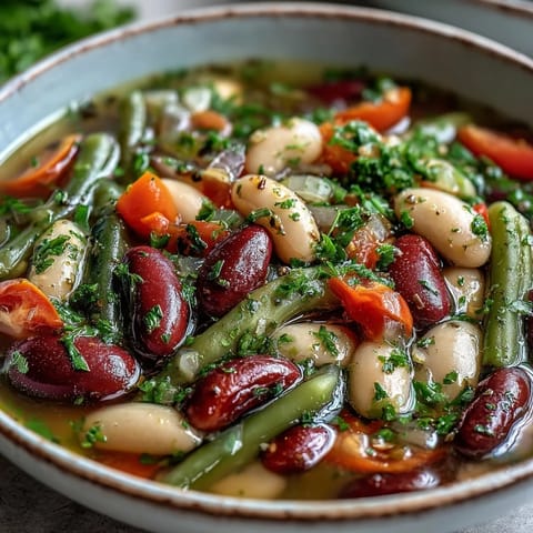 This hearty Three-Bean Salad Soup includes red bell peppers and onions in a savory vegetable broth, perfect for cozy lunches.
