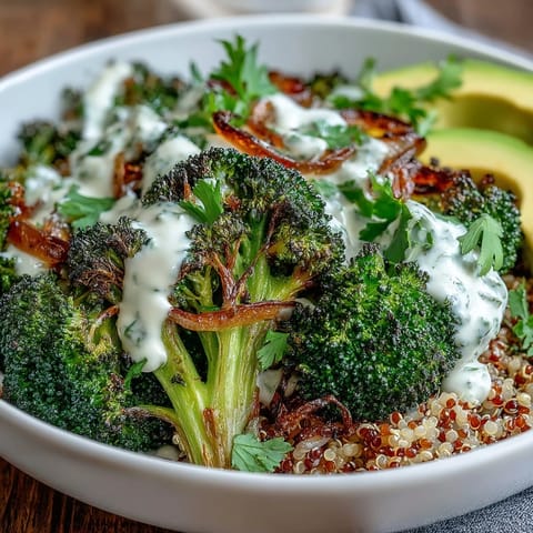 A drizzled creamy tahini sauce and avocado slices top this vibrant vegan Roasted Broccoli Bowl.