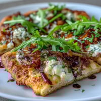 A golden flatbread pizza with sweet caramelized onions, melted mozzarella, tangy goat cheese, and peppery arugula, finished with balsamic glaze.