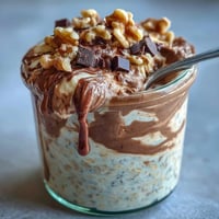 Chunky Monkey Protein Overnight Oats layered in a jar with mashed banana, chocolate chips, and creamy peanut butter swirls.