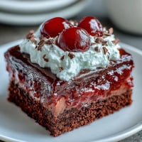 Moist Cherry Cola Jello Poke Cake topped with whipped cream and bright red cherries.